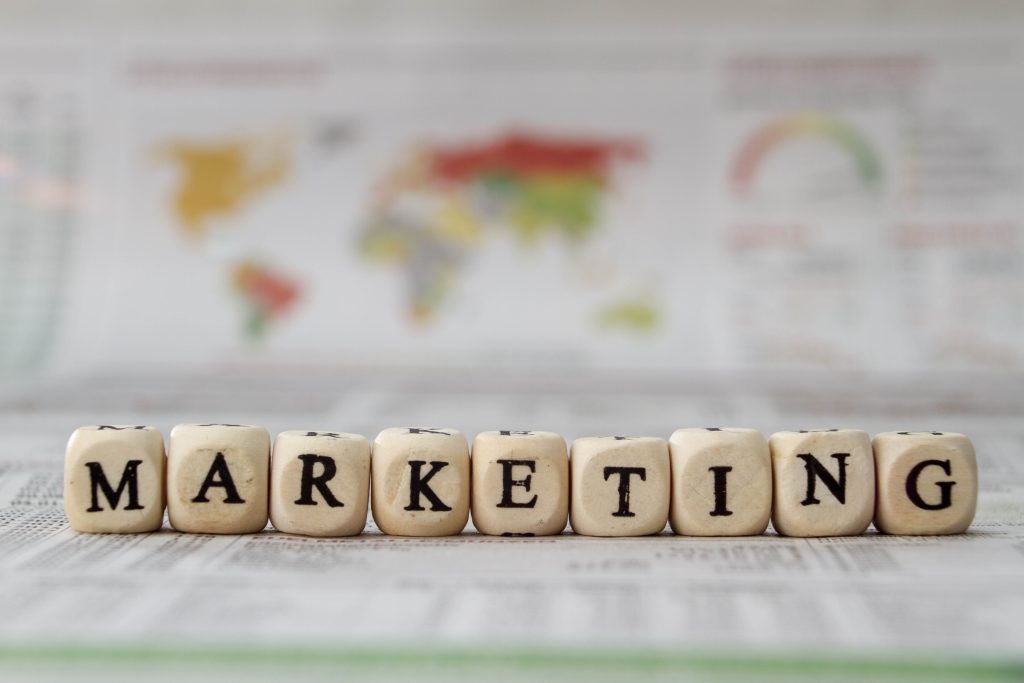 Wooden letter blocks spelling Marketing in front of a blurred world map