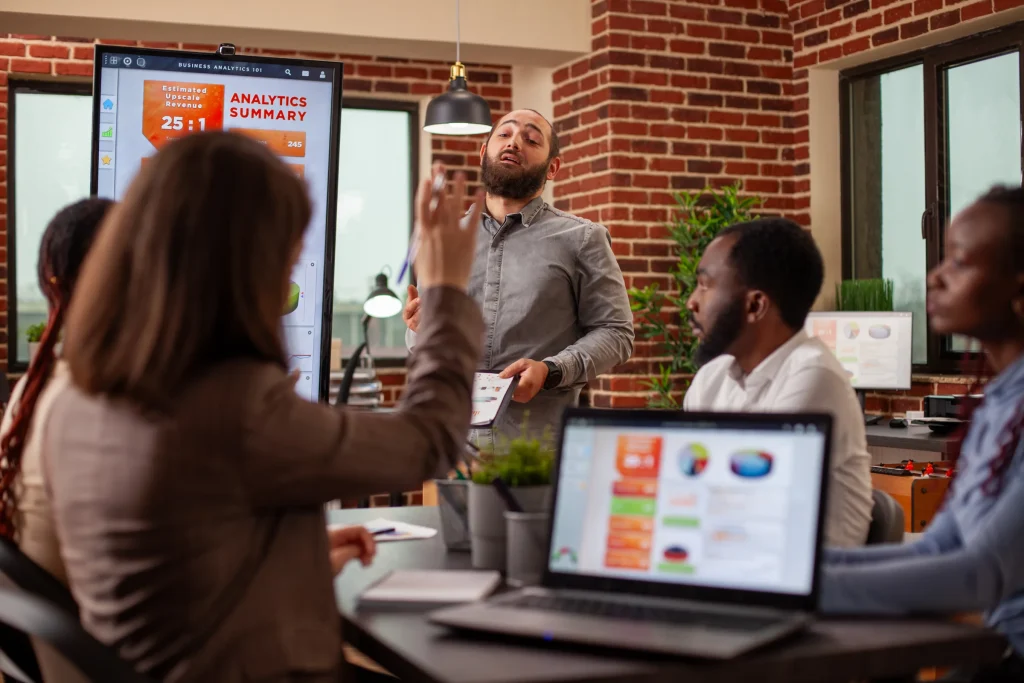 Man presenting analytics charts on a screen to a team in a brick office