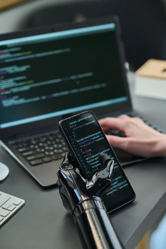 Hands coding on a laptop while a robotic hand holds a phone