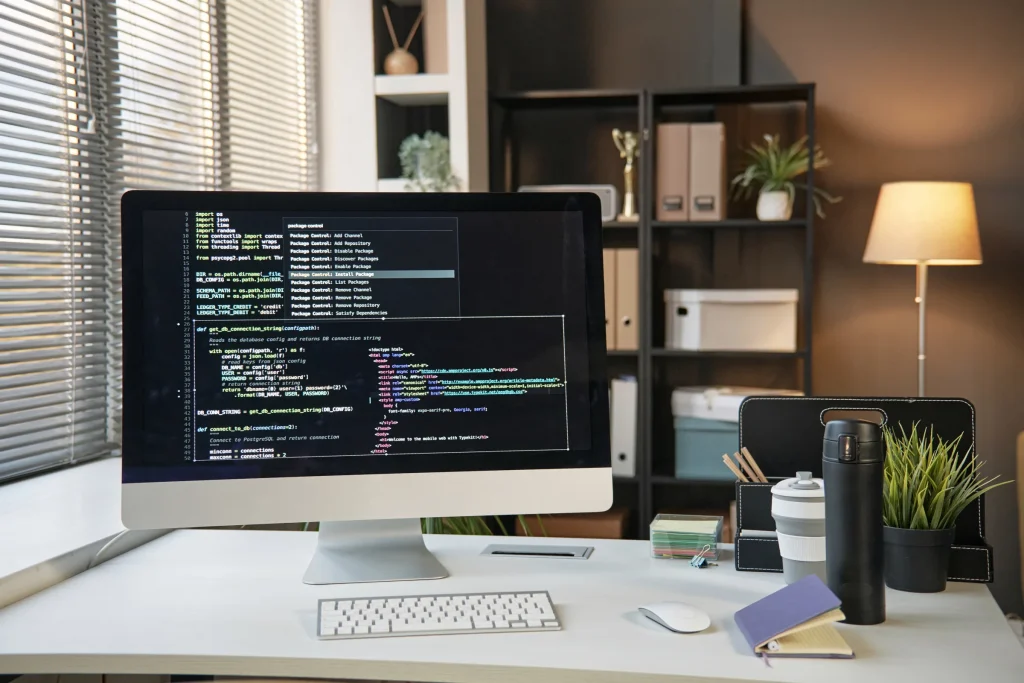 Desktop computer displaying code on an office desk with a lamp and shelves