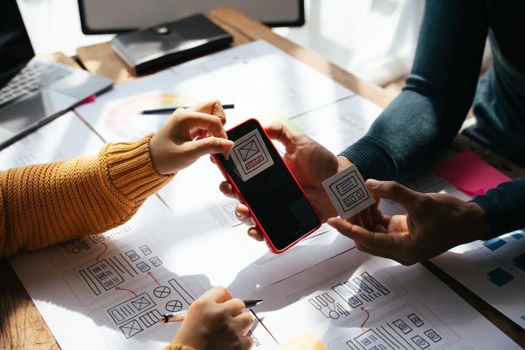 Hands holding a phone scanning a QR code over mobile app wireframe sketches