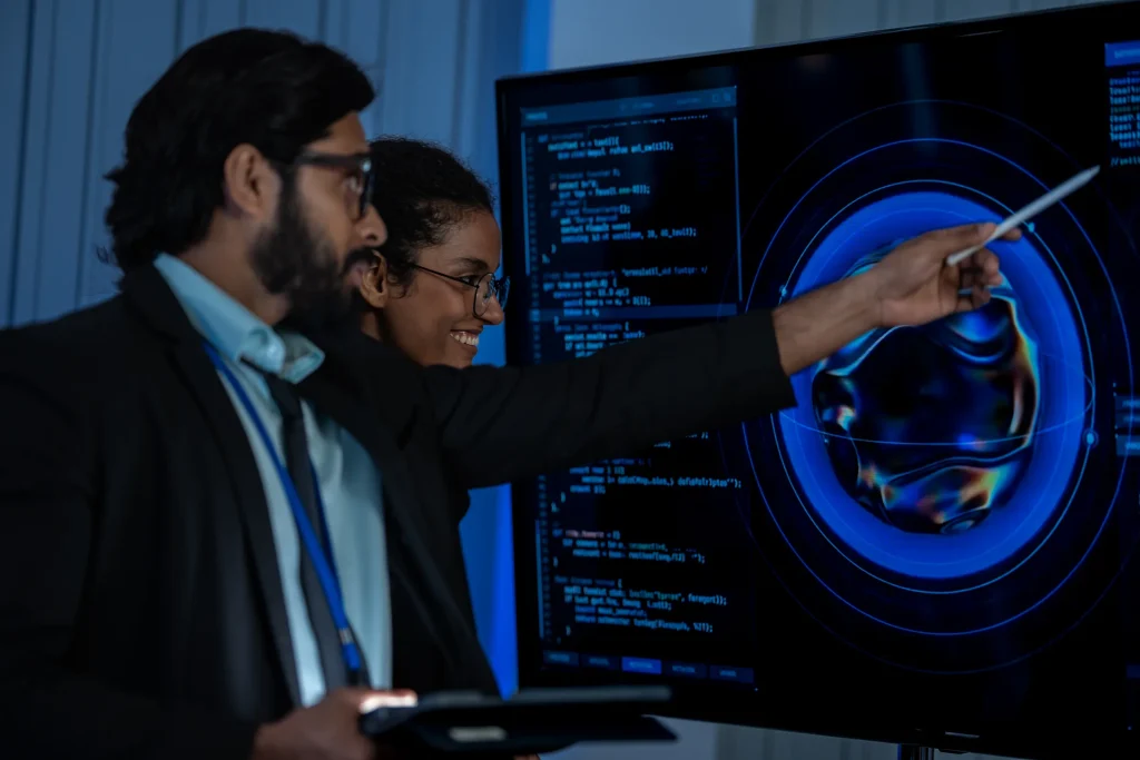 Man and woman pointing at a holographic globe on a large display with code